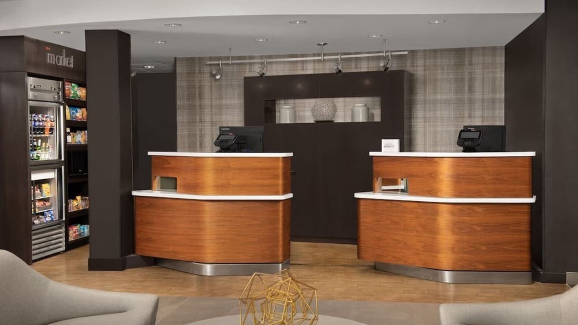 Hotel reception area with two curved wooden front desks, computer terminals, a snack display and modern lounge seating at Courtyard By Marriott Dothan.