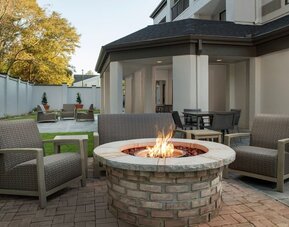 Outdoor patio with cushioned lounge chairs surrounding a circular brick fire pit, with lawn and landscaping at Courtyard By Marriott Dothan.