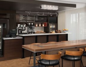 Refreshment station with coffee machines, refrigerated drinks, pastries, fruit and a long communal wooden table at Courtyard By Marriott Dothan.
