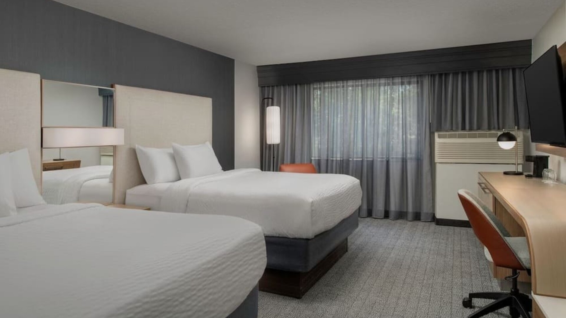 Guest room with two white beds, mirrored headboard panels, wooden desk, office chair, television and curtained window at Courtyard By Marriott Dothan.