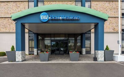 Hotel entrance beneath a blue and green Best Western canopy, with glass doors and planters at Best Western Executive Hotel Of New Haven-West Haven.
