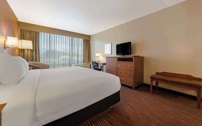 Guest room with king bed, wooden dresser, television, desk and large curtained window at Best Western Executive Hotel Of New Haven-West Haven.