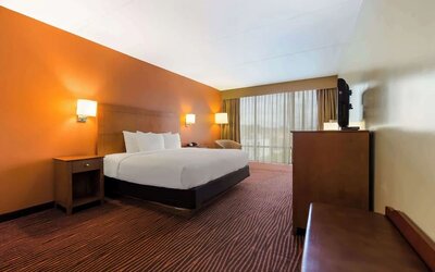 Guest room with king bed, wooden furniture, desk, television and large curtained window at Best Western Executive Hotel Of New Haven-West Haven.