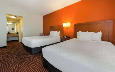 Guest room with two beds, orange accent wall, wooden headboards and bedside lighting at Best Western Executive Hotel Of New Haven-West Haven.