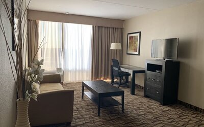 Lounge area with beige sofa, dark coffee table, television and large windows at Best Western Executive Hotel Of New Haven-West Haven.