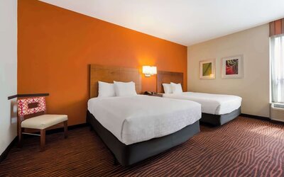 Guest room with two beds, orange accent wall, patterned carpet and a wooden chair at Best Western Executive Hotel Of New Haven-West Haven.