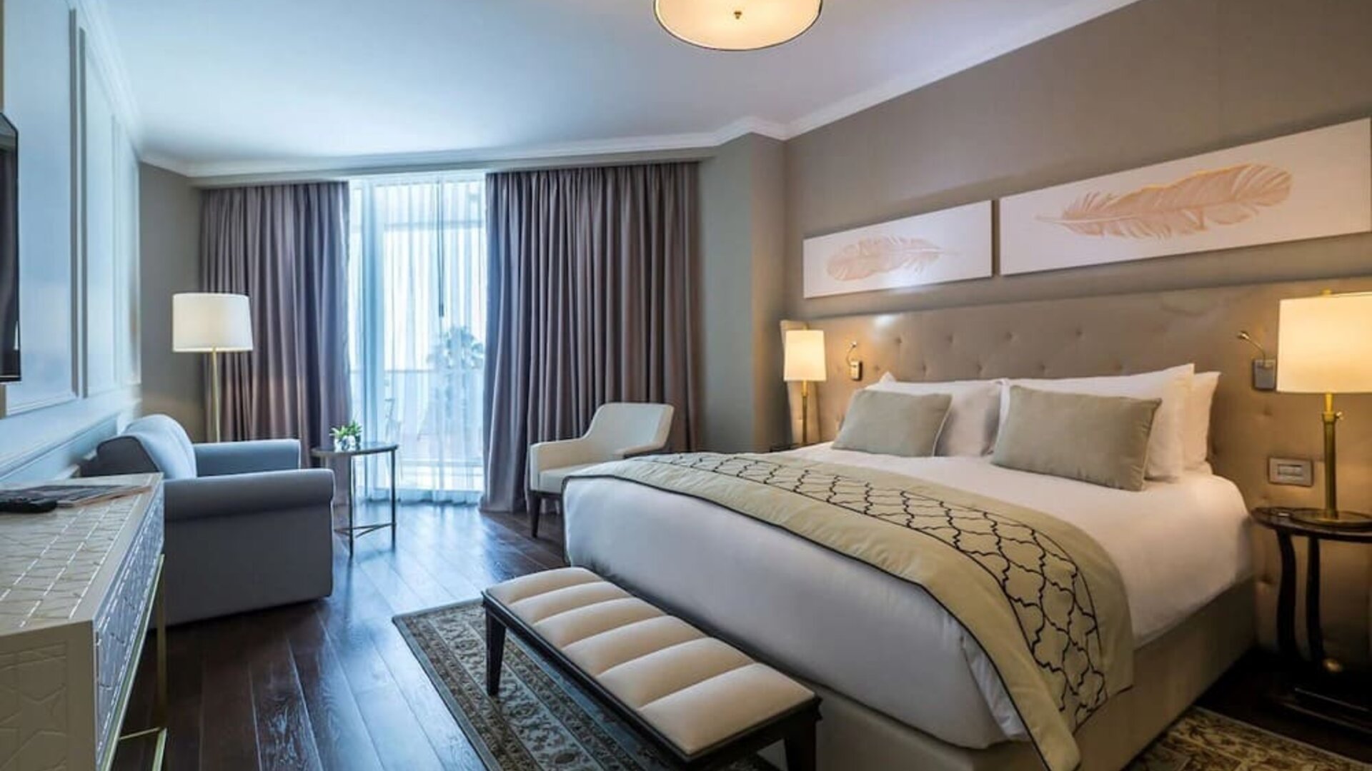 Guest room with king bed, upholstered headboard, bedside lamps, seating area and large curtained windows at David Tower Hotel Netanya.