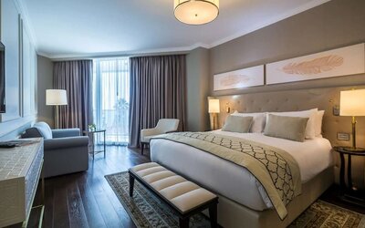Guest room with king bed, upholstered headboard, bedside lamps, seating area and large curtained windows at David Tower Hotel Netanya.