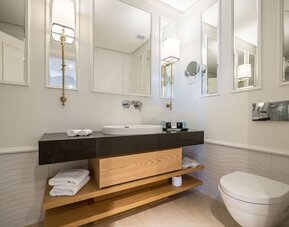 Modern bathroom with dark vanity, white basin, illuminated mirrors, folded towels and wall-mounted toilet at David Tower Hotel Netanya.