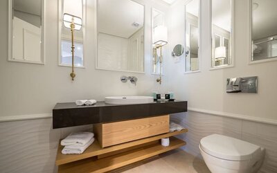 Modern bathroom with dark vanity, white basin, illuminated mirrors, folded towels and wall-mounted toilet at David Tower Hotel Netanya.