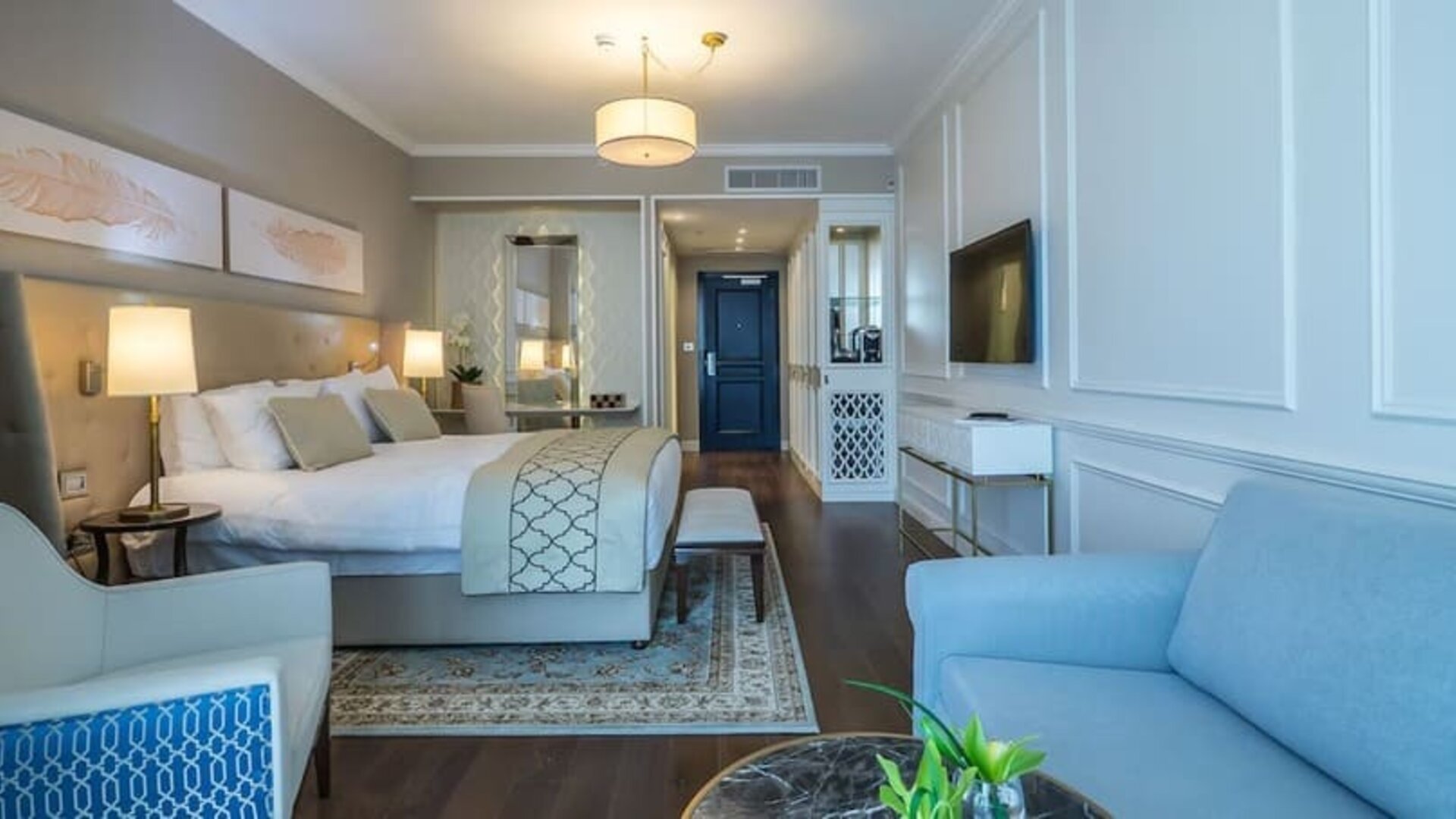 Spacious suite with a king bed, blue sofa, white armchair, coffee table and separate sitting area at David Tower Hotel Netanya.