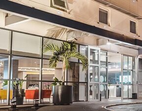 Hotel entrance at night with glass frontage, illuminated signage, palm planters and colourful lounge seating visible inside at Novotel Lima San Isidro.