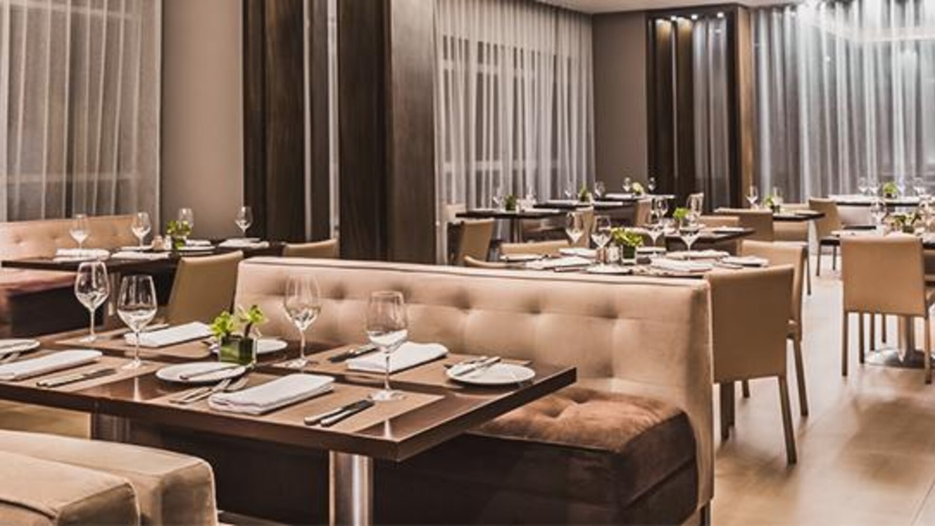 Hotel dining room with neatly arranged tables, upholstered seating, floor-to-ceiling windows and soft lighting at Novotel Lima San Isidro.