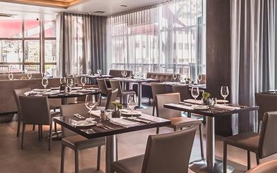 Hotel restaurant with neatly arranged dining tables, upholstered chairs, floor-to-ceiling windows and curtains at Novotel Lima San Isidro.