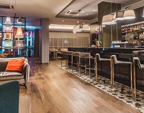 Hotel bar with dark leather sofas, colorful accent cushions, upholstered chairs, high stools and illuminated shelving at Novotel Lima San Isidro.