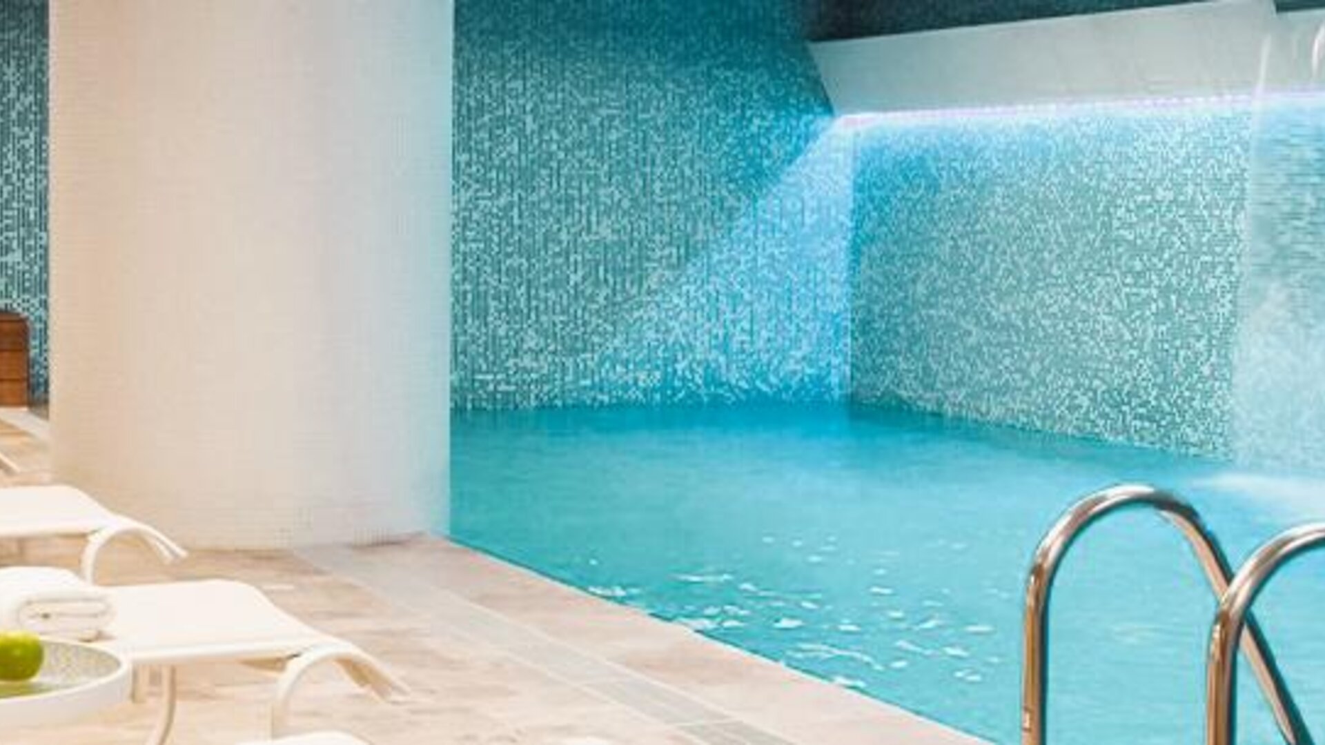 Indoor swimming pool with turquoise water, mosaic-tiled walls and white loungers along the poolside at Novotel Lima San Isidro.