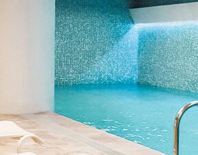 Indoor swimming pool with turquoise water, mosaic-tiled walls and white loungers along the poolside at Novotel Lima San Isidro.