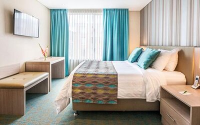 Guest bedroom with king bed, teal cushions, patterned bed runner, wall-mounted television and bedside tables at Apartamentos Plaza Suites.