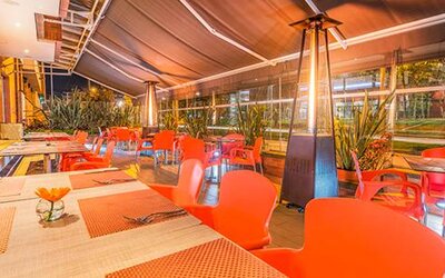 Covered outdoor dining terrace with tables, bright red chairs, patio heaters and floor-to-ceiling windows at Apartamentos Plaza Suites.