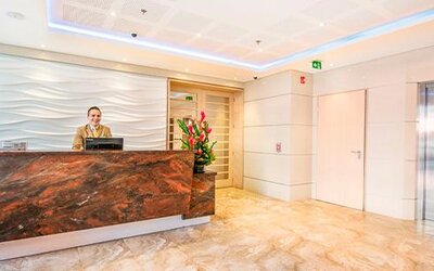Hotel reception area with a dark marble-front desk, reception staff, flower arrangement and elevator at Apartamentos Plaza Suites.