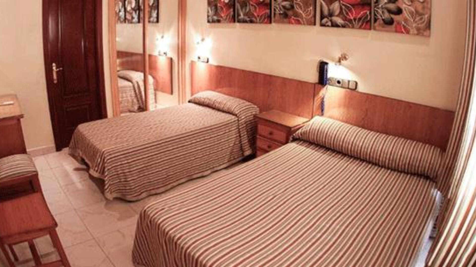 Twin room with two single beds, matching striped bedspreads, bedside tables, wall lights and a full-length mirror at Hostal Atocha Almudena Martín.