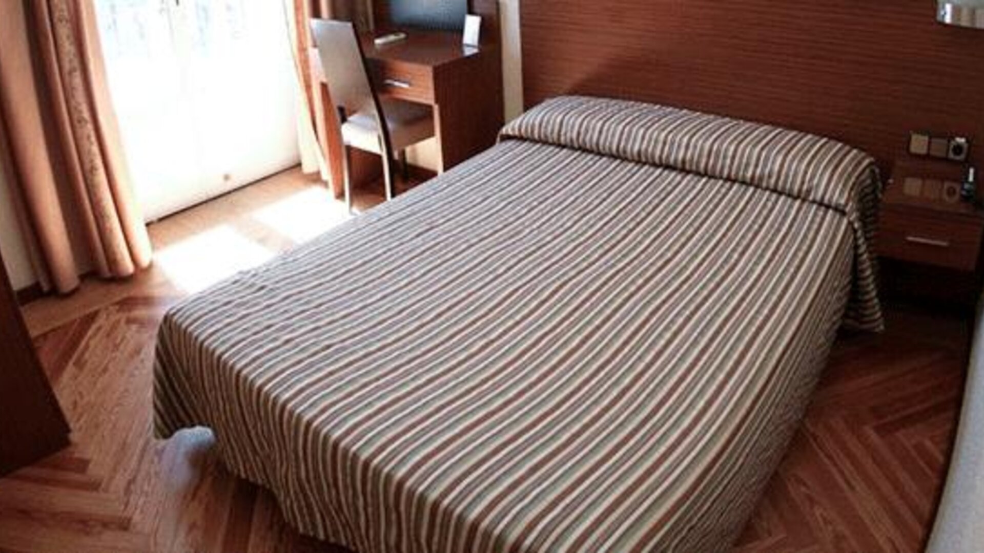 Guest room with a double bed, striped bedding, wooden flooring, desk and bright window at Hostal Atocha Almudena Martín.