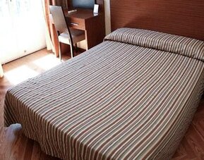 Guest room with a double bed, striped bedding, wooden flooring, desk and bright window at Hostal Atocha Almudena Martín.
