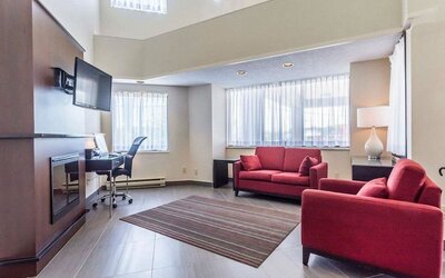 Lobby lounge area with fireplace and workspace with computer, printer and ergonomic chair at Comfort Inn Thetford Mines. 