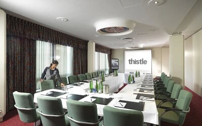 Room for business meetings with large windows, screen, and seating around single table for around a dozen people.