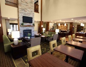 The hotel’s lounge is furnished with armchair and sofa seating around coffee tables, with a wall-mounted TV, and more tables and chairs nearby.