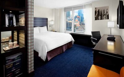 King bedroom with TV, work station and a view of the city at Hilton New York Fashion District.