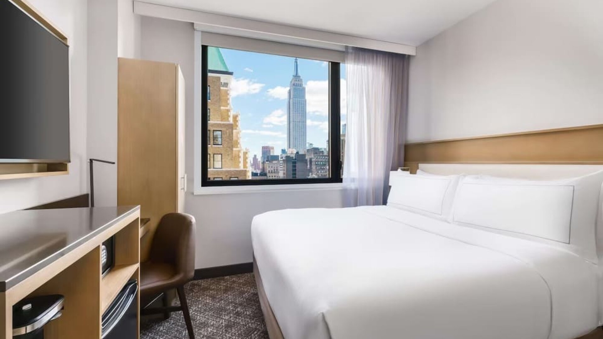 Guest room in the DoubleTree Times Square South, with a bed, beautiful view of the city and workspace desk and chair.