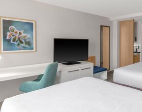 Workspace area at Hilton Garden Inn Queens/JFK Airport with desk, chair, TV and wall art.