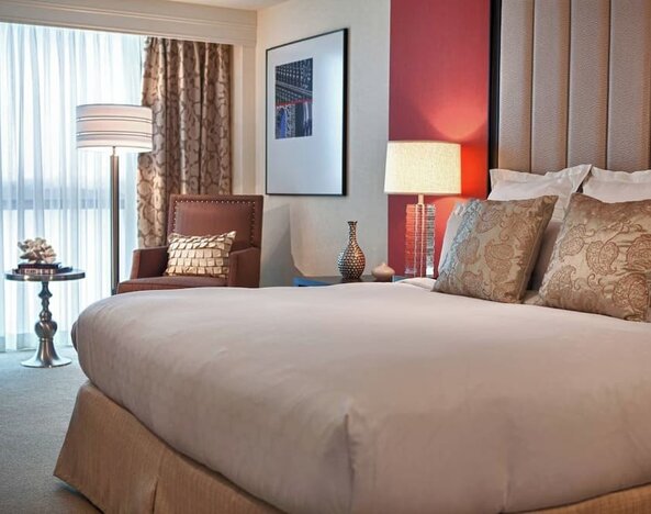 Guest room with king bed, accent pillows, armchair, floor lamp, and window seating area at Renaissance Newark Airport Hotel.