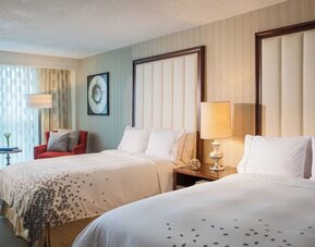 Guest room with two double beds, bedside lamp, armchair, and sheer curtains at Renaissance Newark Airport Hotel.