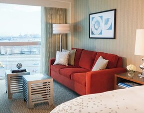 Guest room seating area with red sofa, coffee table, large window view, and bedside lamp at Renaissance Newark Airport Hotel.