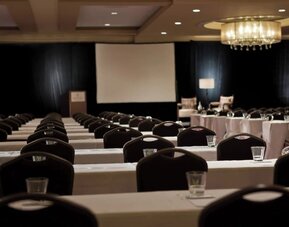 Conference room with rows of tables and chairs facing projector screen and podium at Renaissance Newark Airport Hotel.