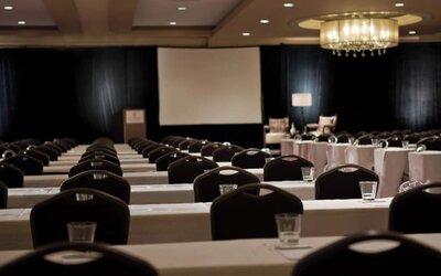 Conference room with rows of tables and chairs facing projector screen and podium at Renaissance Newark Airport Hotel.