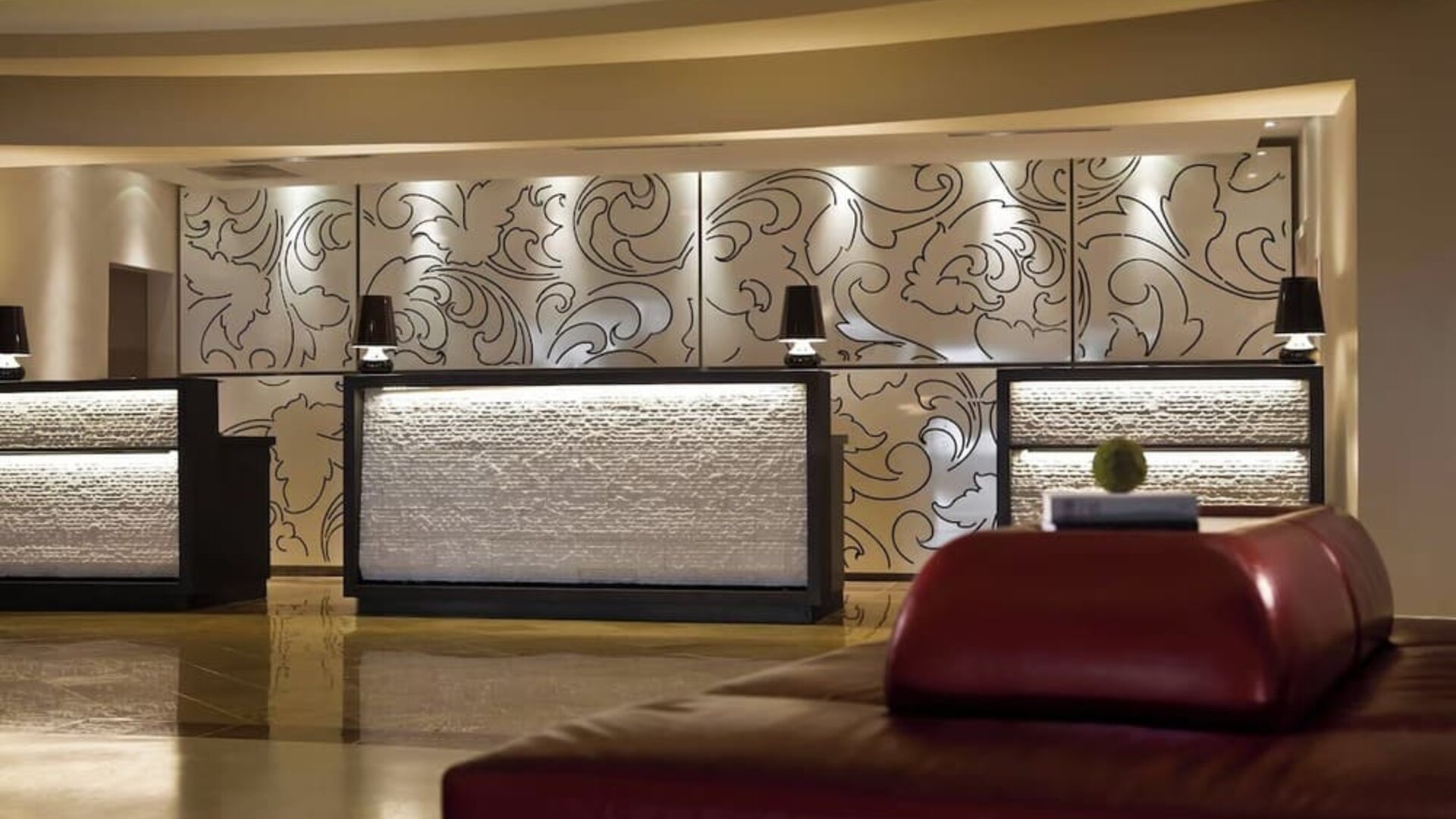 Lobby reception desks with decorative wall panels, warm lighting, and seating at Renaissance Newark Airport Hotel.