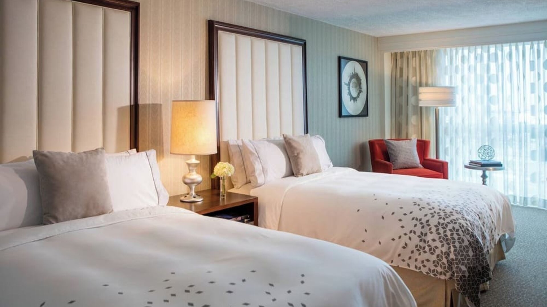 Guest room with two beds, bedside table, lamp, armchair, and window with curtains at Renaissance Newark Airport Hotel.