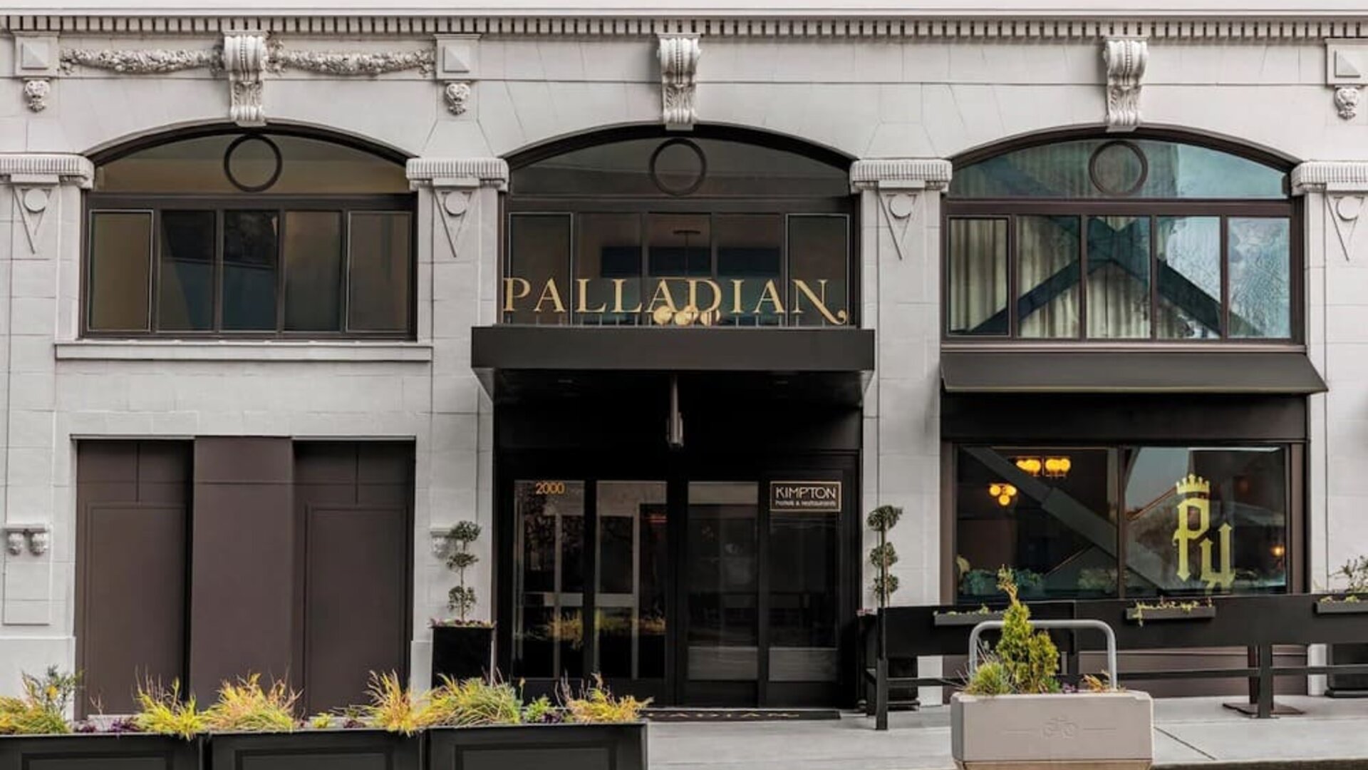 Hotel entrance with black awning, signage, and planters along sidewalk at Kimpton Palladian Hotel.