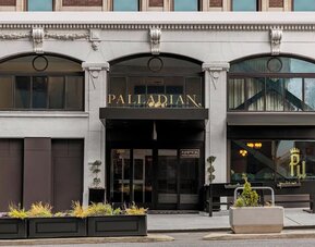Hotel entrance with black awning, signage, and planters along sidewalk at Kimpton Palladian Hotel.