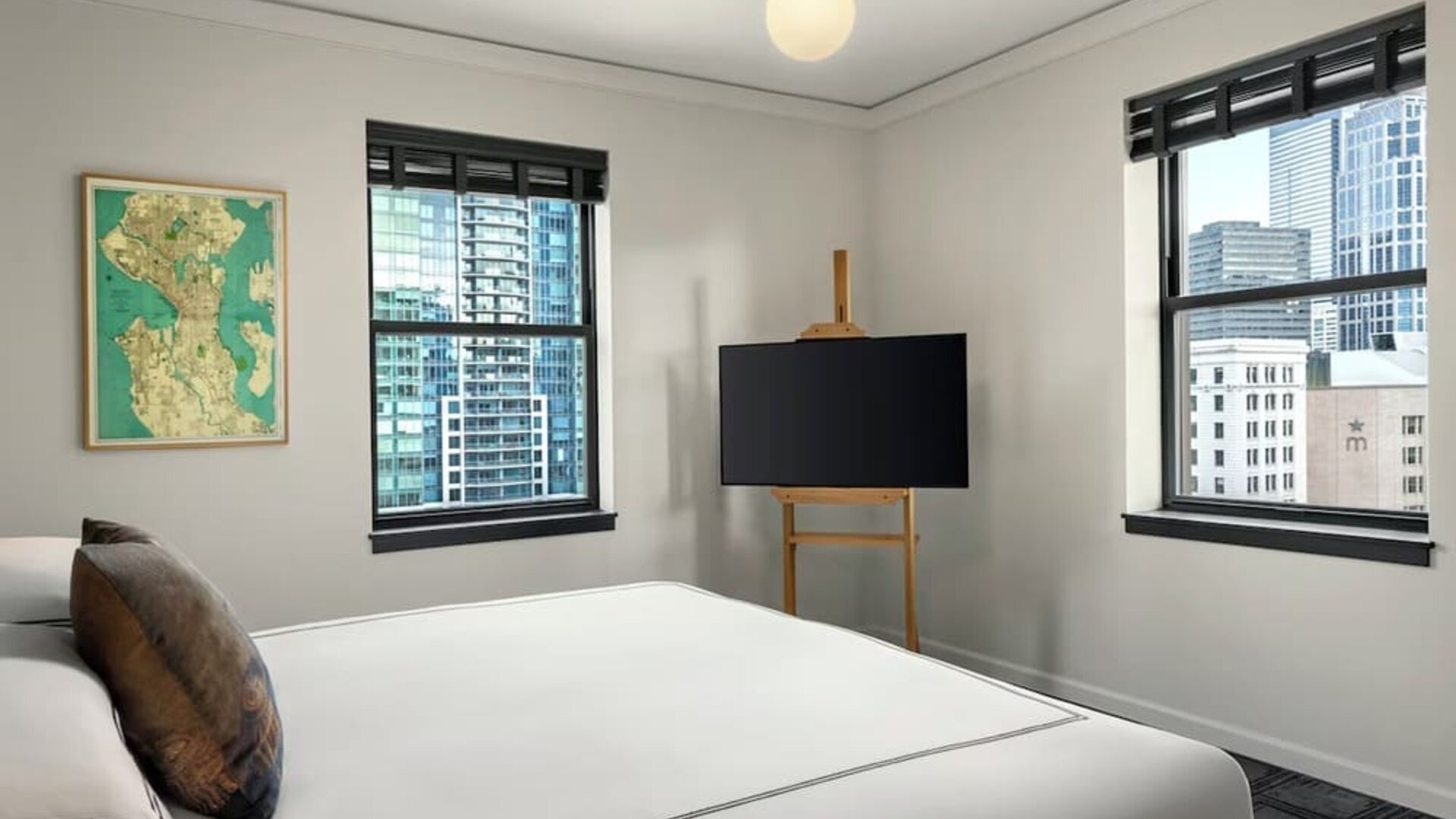 Bedroom with king bed, two windows showing city buildings, and television on stand at Kimpton Palladian Hotel.