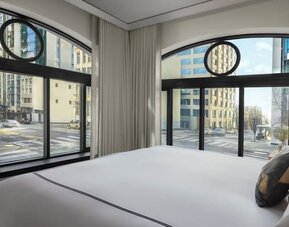 Corner bedroom with large curved windows, city street views, and white bedding at Kimpton Palladian Hotel.