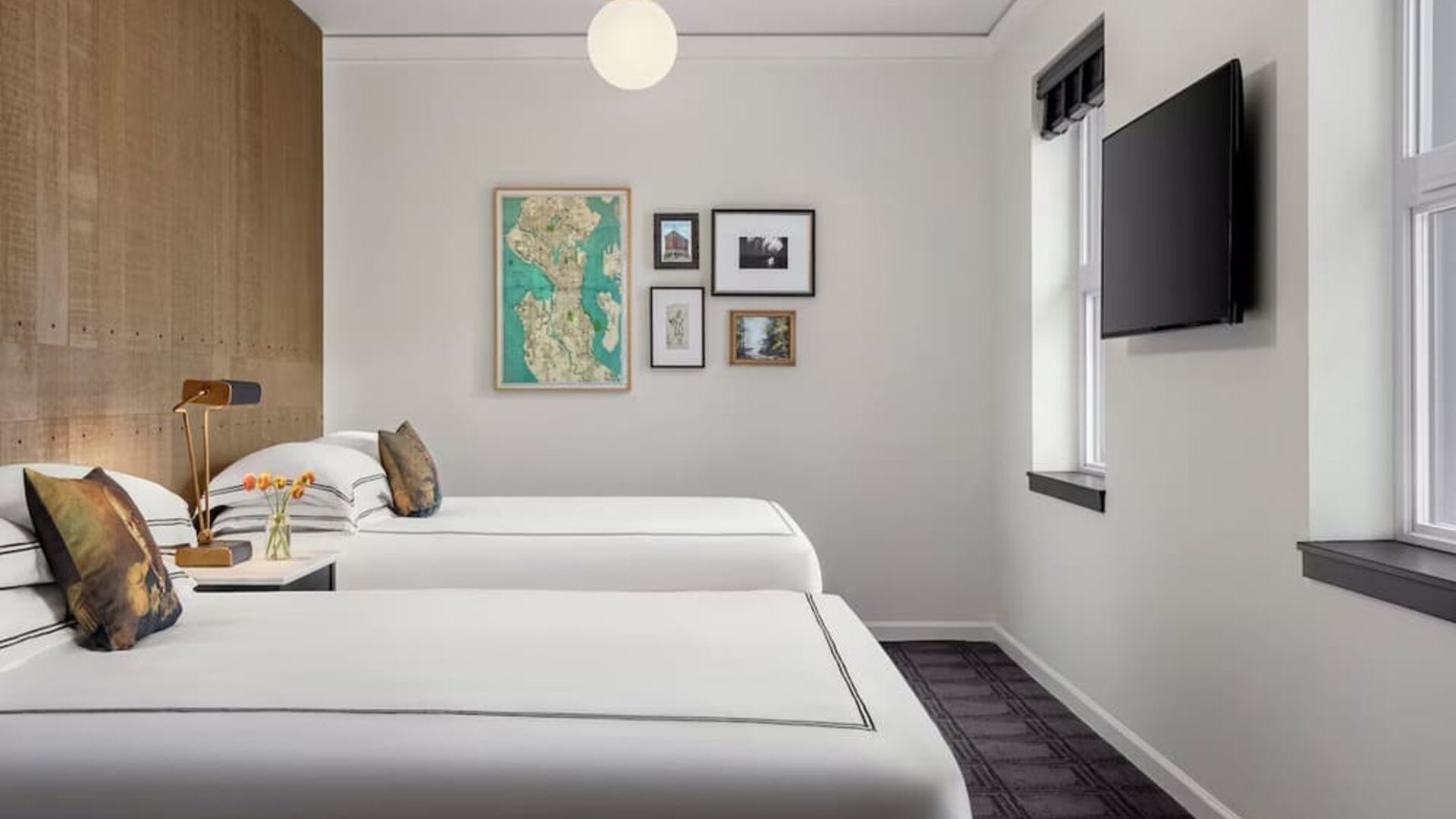 Guest room with two beds, city view windows, and wall-mounted TV in bright interior at Kimpton Palladian Hotel.