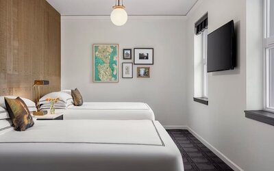 Guest room with two beds, city view windows, and wall-mounted TV in bright interior at Kimpton Palladian Hotel.