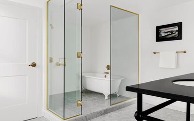 Bathroom with glass shower, freestanding clawfoot tub, white tile walls, and brass fixtures at Kimpton Palladian Hotel.