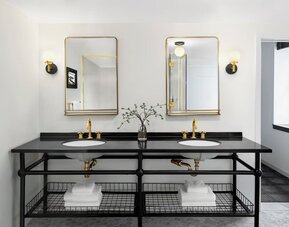 Double vanity bathroom with black countertop, gold fixtures, twin mirrors, and towels at Kimpton Palladian Hotel.
