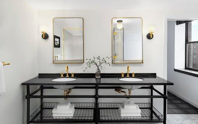 Double vanity bathroom with black countertop, gold fixtures, twin mirrors, and towels at Kimpton Palladian Hotel.