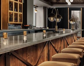 Long marble bar counter with upholstered stools, pendant lighting, and liquor shelves at Kimpton Palladian Hotel.
